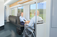 Skisse fra innsiden av de nye togene, der en rullestolbruker og en annen passasjer sitter og snakker sammen.