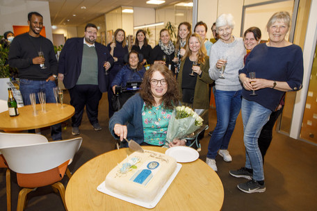 Magnhild Sørbotten skjærer et stykke kake mens ansatte står bak og smiler.