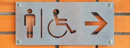 Bilde av toalettskilt på en murvegg. Med herre-symbol og rullestolsymbol.