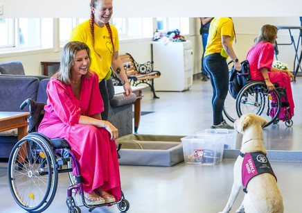 Märtha Louise sitter i en rullestol og smiler mot en hund som med 