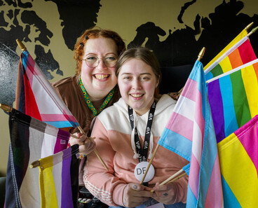 De to poserer med en mengde flagg som representerer ulike skeive identiteter.