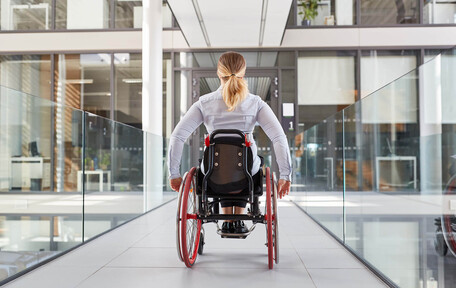 Ung kvinne i rullestol på vei mot inngangsdøren til en kontorbygning.