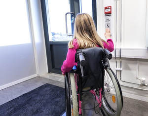 Barn i rullestol som åpner en dør.