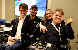 Tre menn og en kvinne med spillkontroller foran stor TV-skjerm med Super Mario