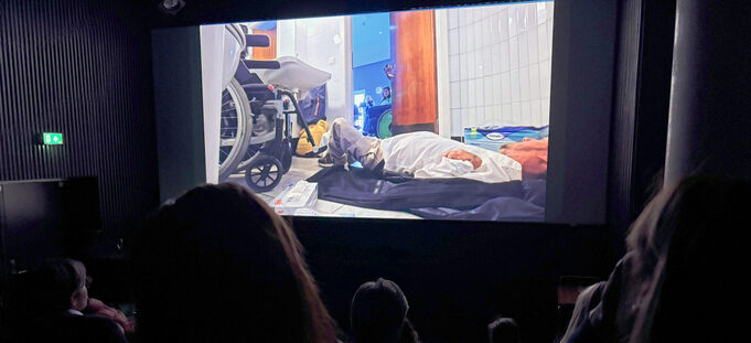 Publikum i mørk kinosal ser film om funksjonshemmet mann på toalettgulv