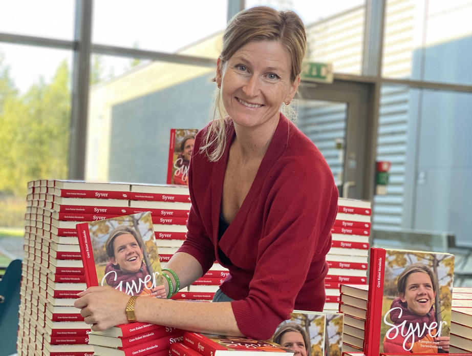 Guro Kulset Merakerås sitter på en bokstabel og holder frem boka om Syver Blindheim