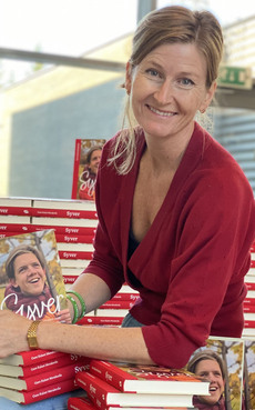 Guro Kulset Merakerås sitter på en bokstabel og holder frem boka om Syver Blindheim