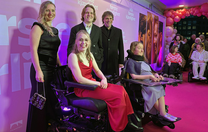 To kvinner i rullestol, foran to menn og en kvinne, alle pent kledd, på rød løper