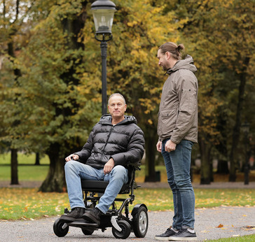 Mann på el-rullestol i park sammen med gående mann