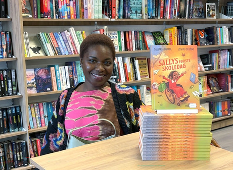Salamatu Kamara ved et bord med en stabel av hennes egen bok