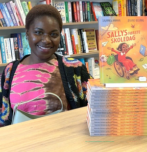 Salamatu Kamara ved et bord med en stabel av hennes egen bok