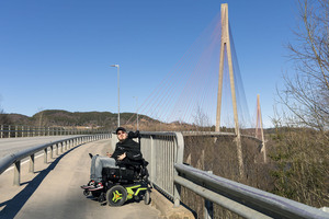 Ørjan Brevik smilende i rullestol foran Skarnsundbrua