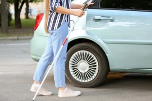 Detaljbilde av kvinne med hvit mobilitetsstokk som åpner bakdøren på en bil.