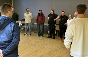 En stor gruppe mennesker står i ring i et seminarrom