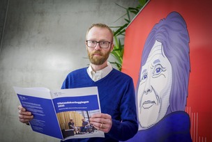 Skogseth med rapporten foran et portrettbilde av Skansgård på en plakat.