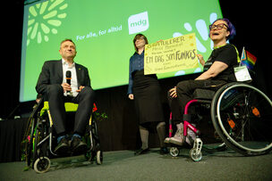 Arild Hermstad i rullestol ved siden av to kvinner med plakaten 