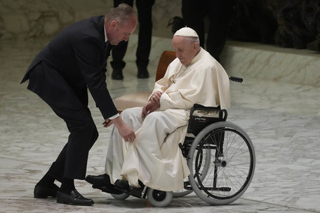 Pave Frans i rullestol får hjelp av en assistent til å få beinet opp på fotbrettet på rullestolen.