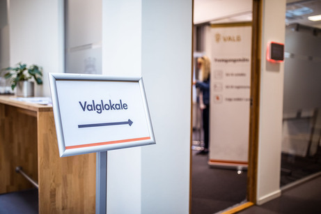 Skilt mot valglokale, valgavlukker i bakgrunnen