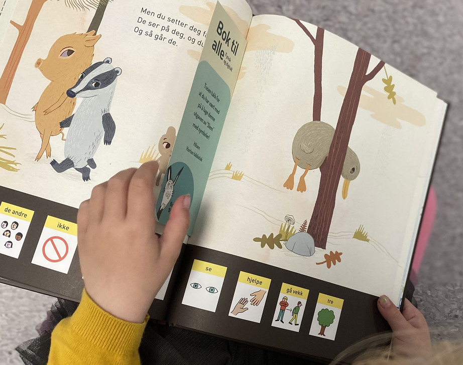 Barnehånd blar i barnebok med symboltegninger nederst på siden