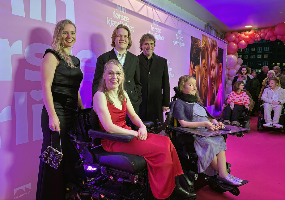 To kvinner i rullestol, foran to menn og en kvinne, alle pent kledd, på rød løper