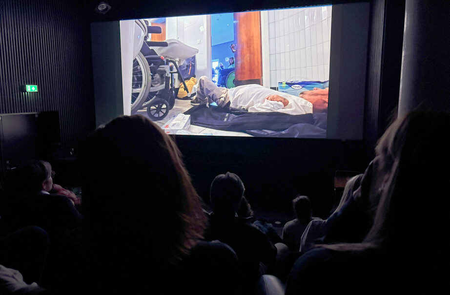 Publikum i mørk kinosal ser film om funksjonshemmet mann på toalettgulv