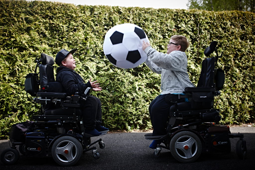 Simen og Daniel sitter i rullestolene og kaster en stor ball mellom seg.