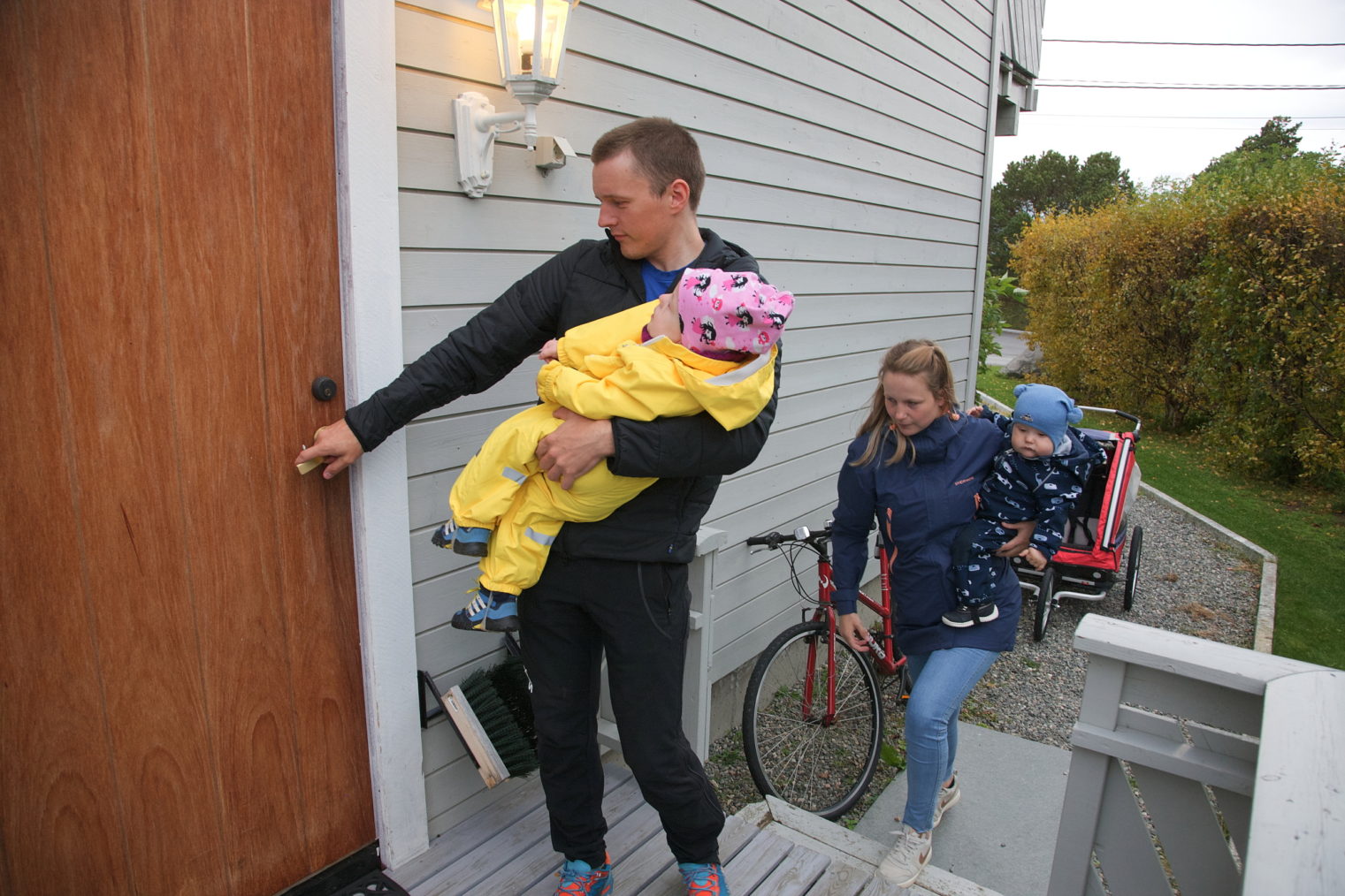 Pappa har Erle på den ene armen mens han åpner inngangsdøren med den andre. Resten av familien følger bak.