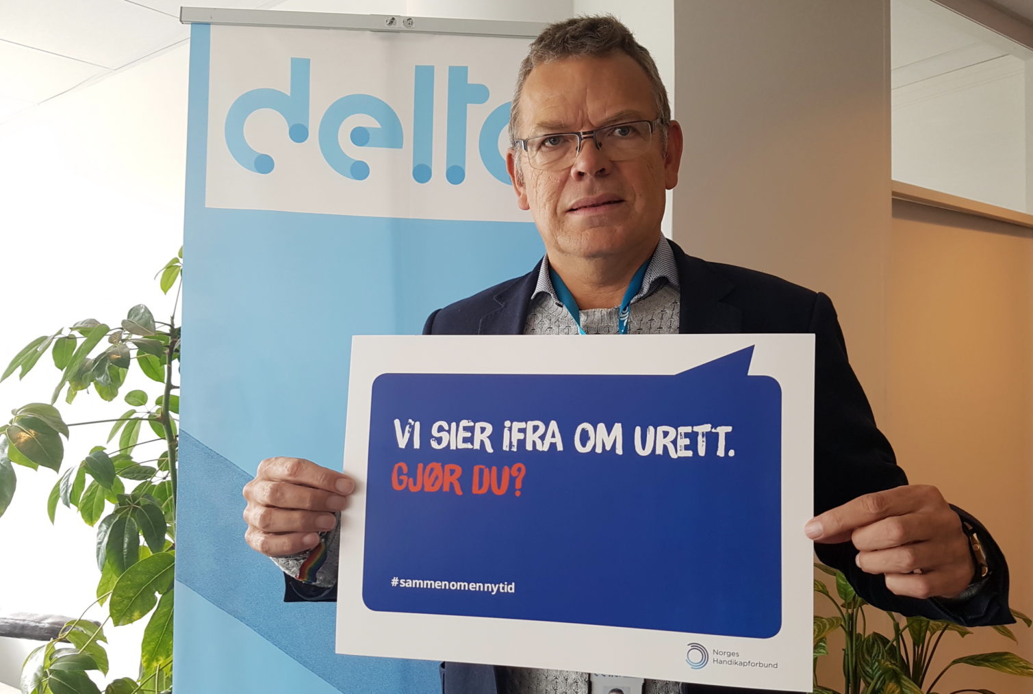 Ellefesen holder fram en av NHFs plakater med teksten «Vi sier fra om urett - gjør du?» I bakgrunnen er Deltas logo på et banner.