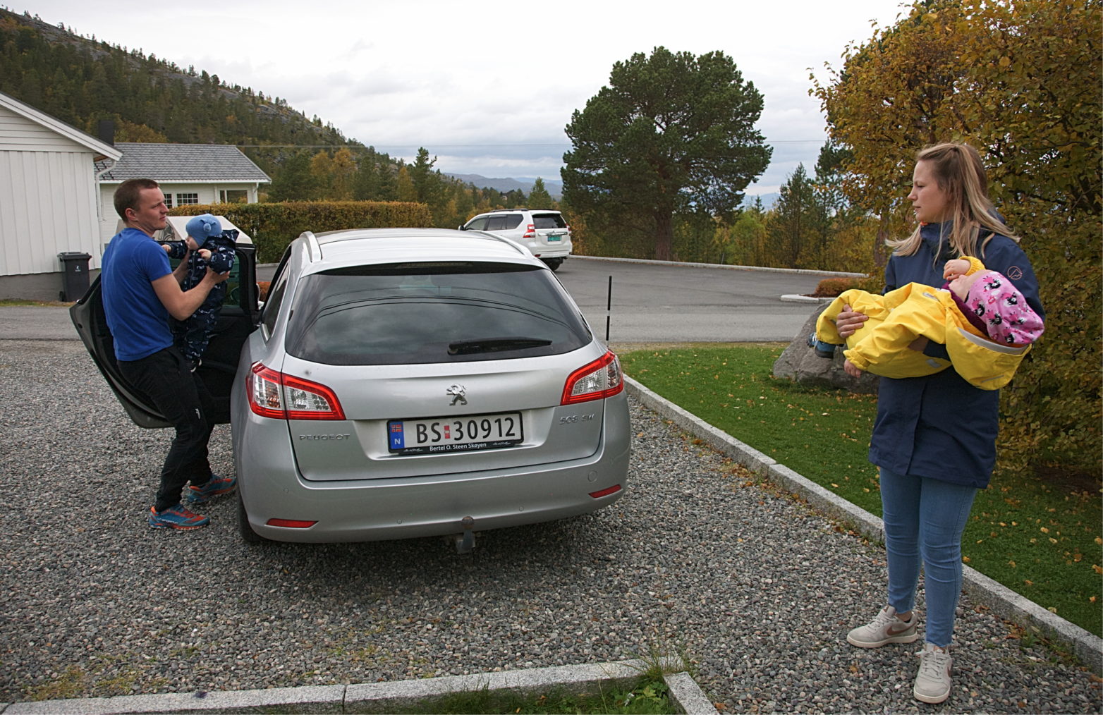 Bilde av foreldrene som bærer hvert sitt barn til bilen.