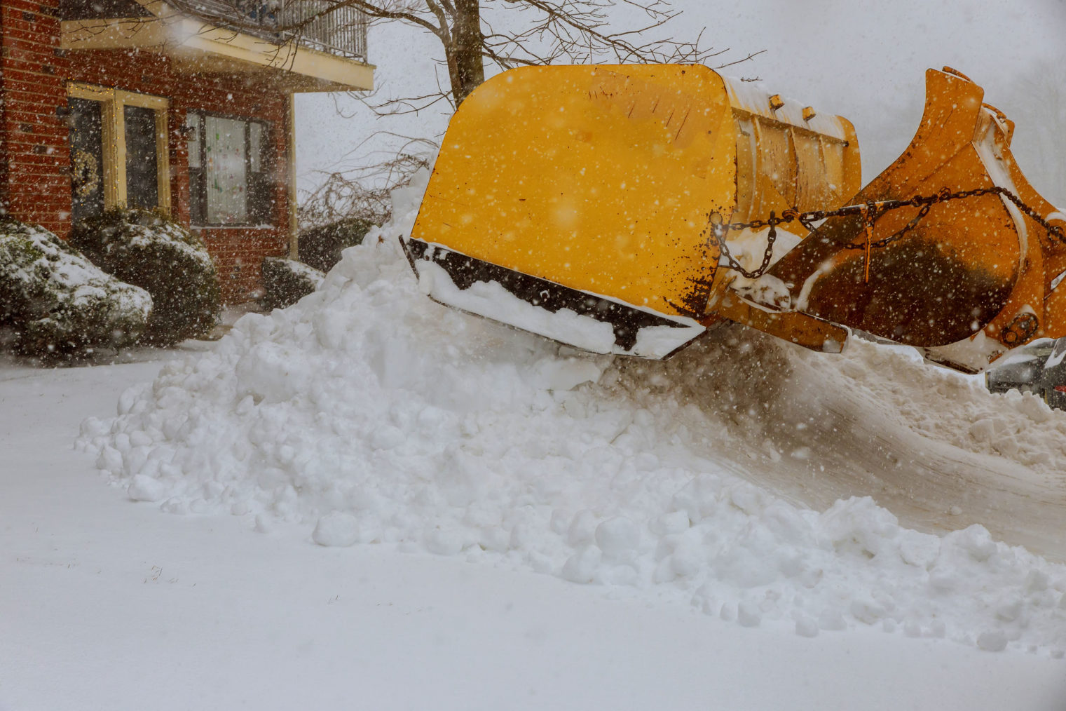 Traktor som måker snø foran et hus.