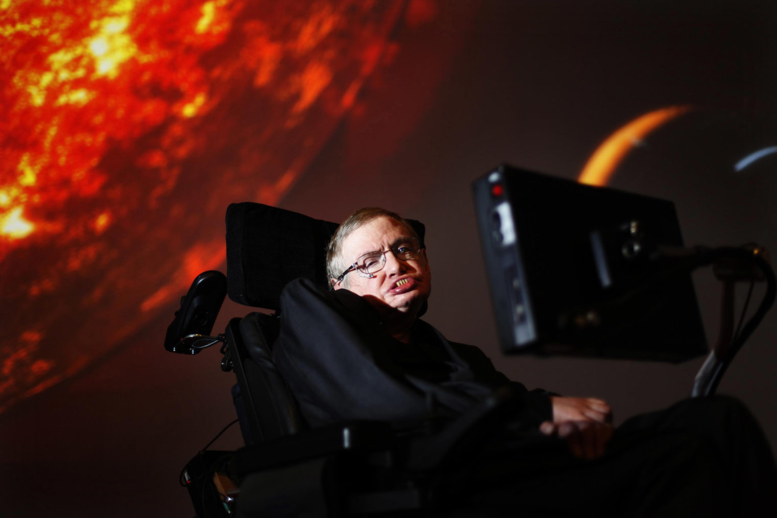 Stephen Hawking fotografert med bilde av et glødende himmellegeme i bakgrunnen.