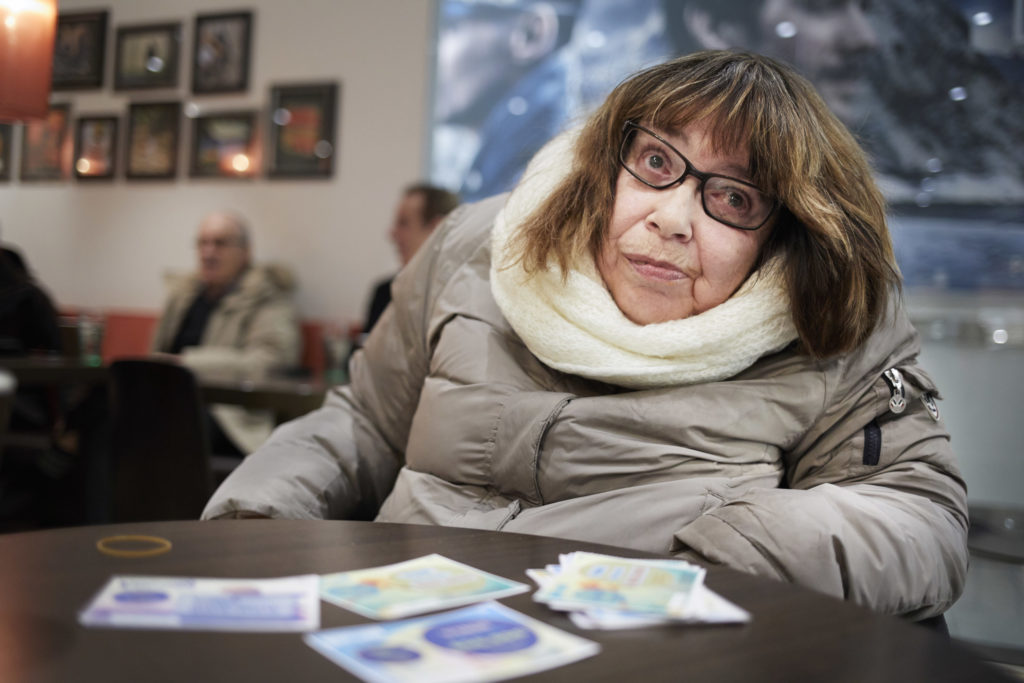 Turid ved kafebord. Loddene ligger på bordet foran henne.