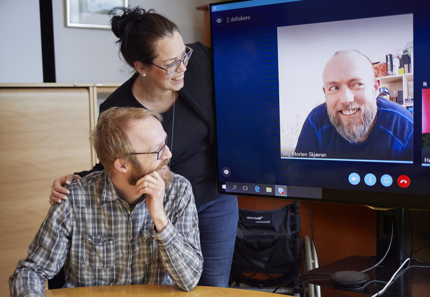 Egil og Hege ved siden av en projektor med Skype-bilde av Stig Morten.