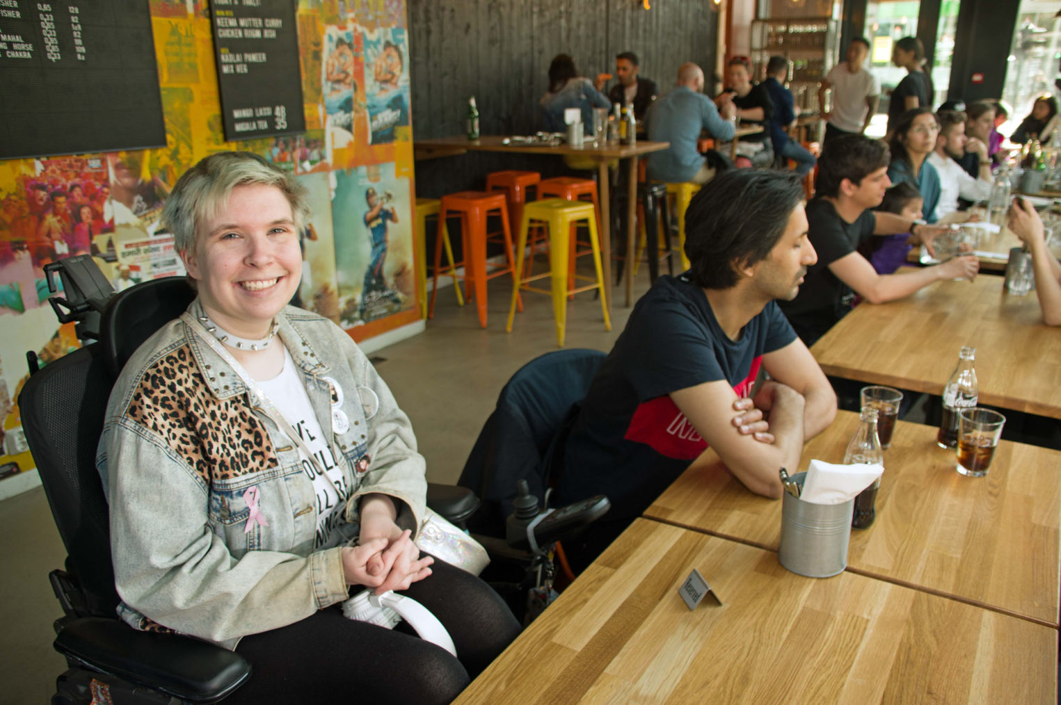 Rina Wesenberg sitter ved et restaurantbord med mange mennesker i bakgrunnen.