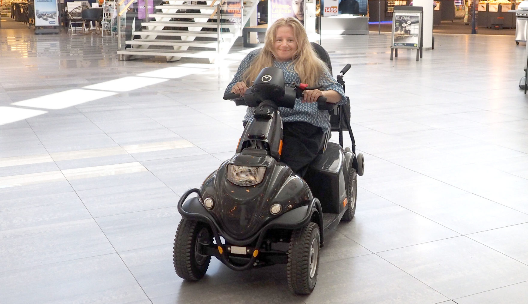 Laila Røynestad på scooteren inne på et kjøpesenter.