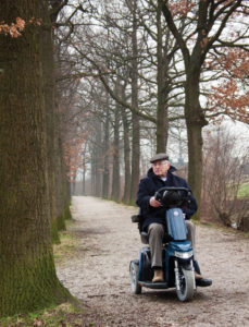 Bilde av eldre mann på scooteren på en vei.