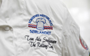 Nærbilde av merket på Steffensens kokkejakke. Tekst: Kokkenes Mesterlaug Sørlandet. Tom Atle Steffensen. The Rolling Chef.