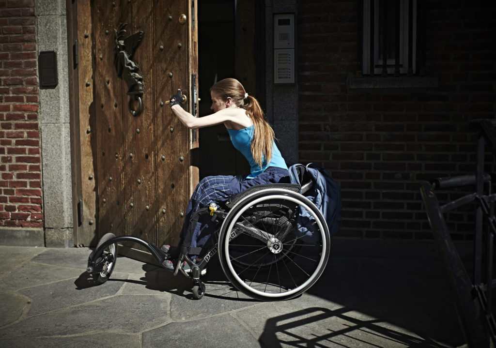 Anne-Maja forsøker å åpne døren sittende i rullestol.