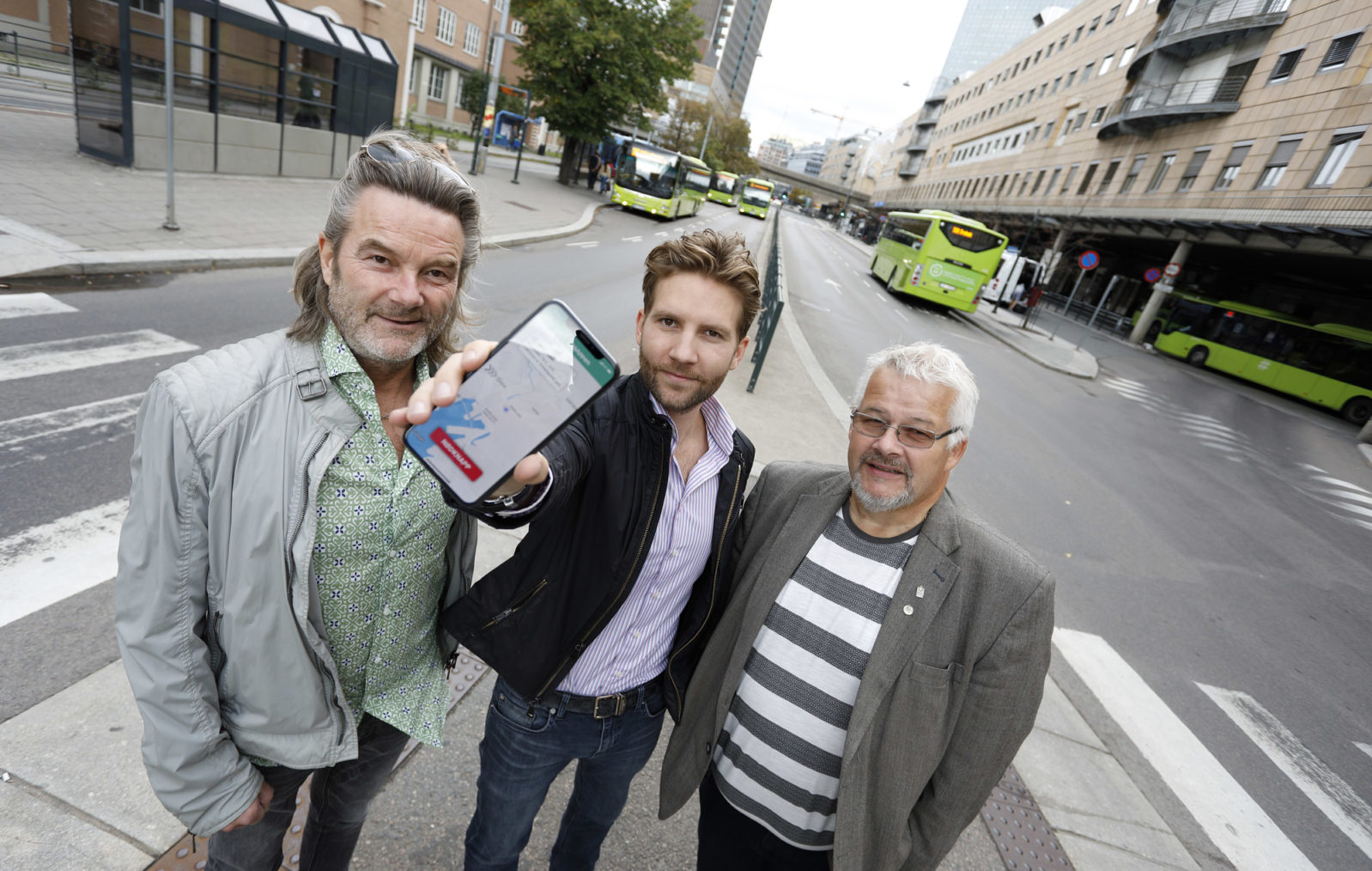 De tre står på gata i Oslo og holder fram en telefon som viser appen.