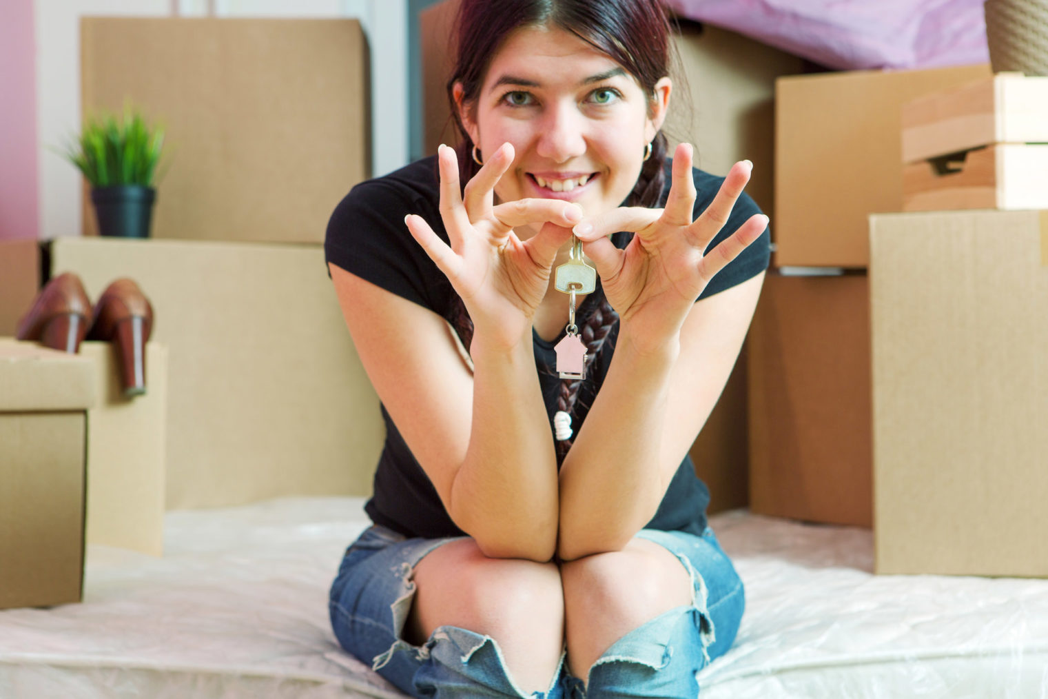 Illustrasjonsbilde av ung kvinne som sitter ved et flyttelass med husnøkler i hendene.