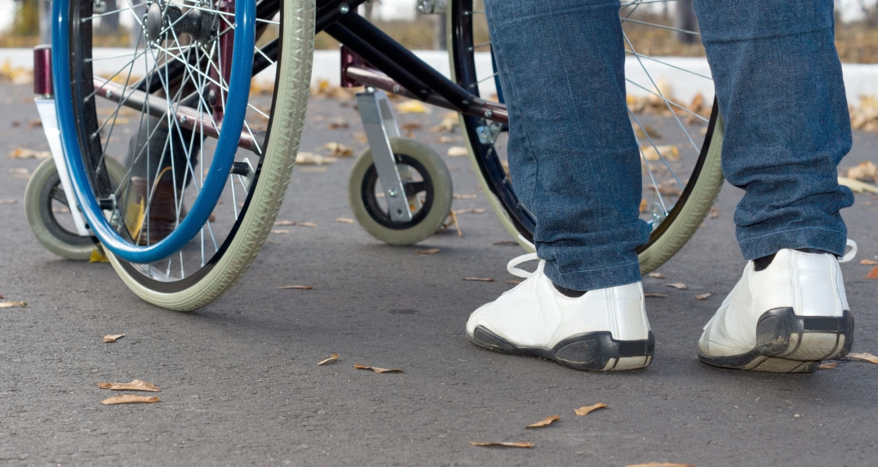 Detaljbilde av beina til en person som dytter en rullestol.