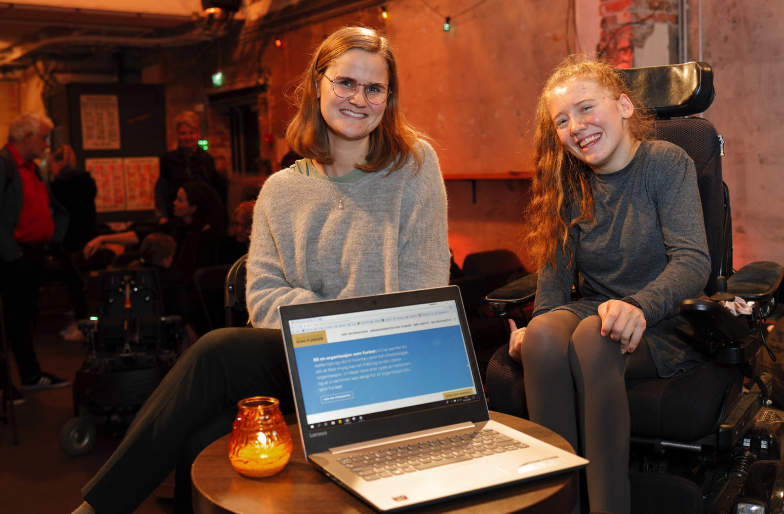 Henriette og Ida sammen ved en pc. I bakgrunnen er folk i salen på