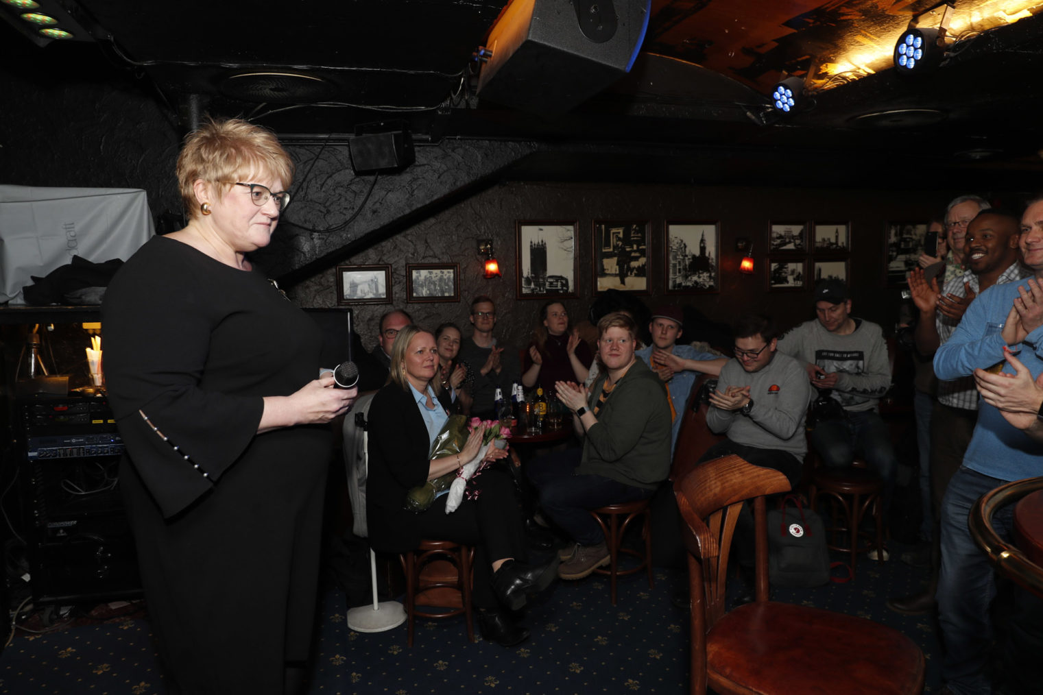 Grande fotografert foran jublende og klappende mennesker på London pub.