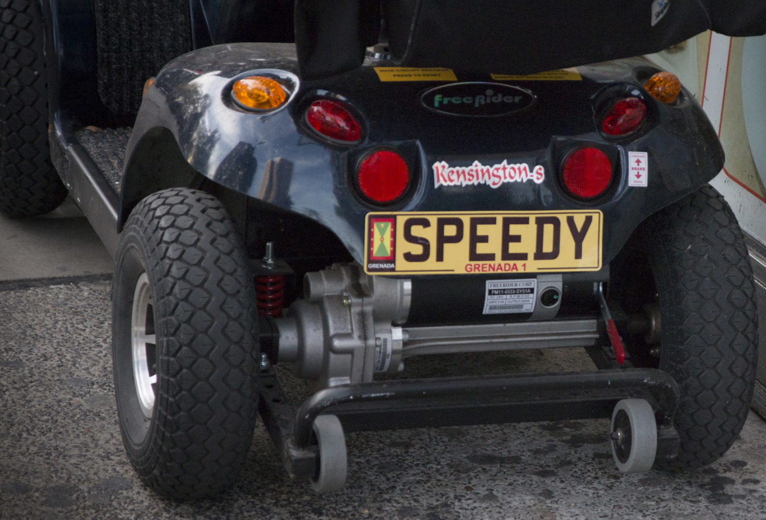 Detaljbilde av baksiden på en elektrisk rullestol, med «bilskilt» med teksten «Speedy»