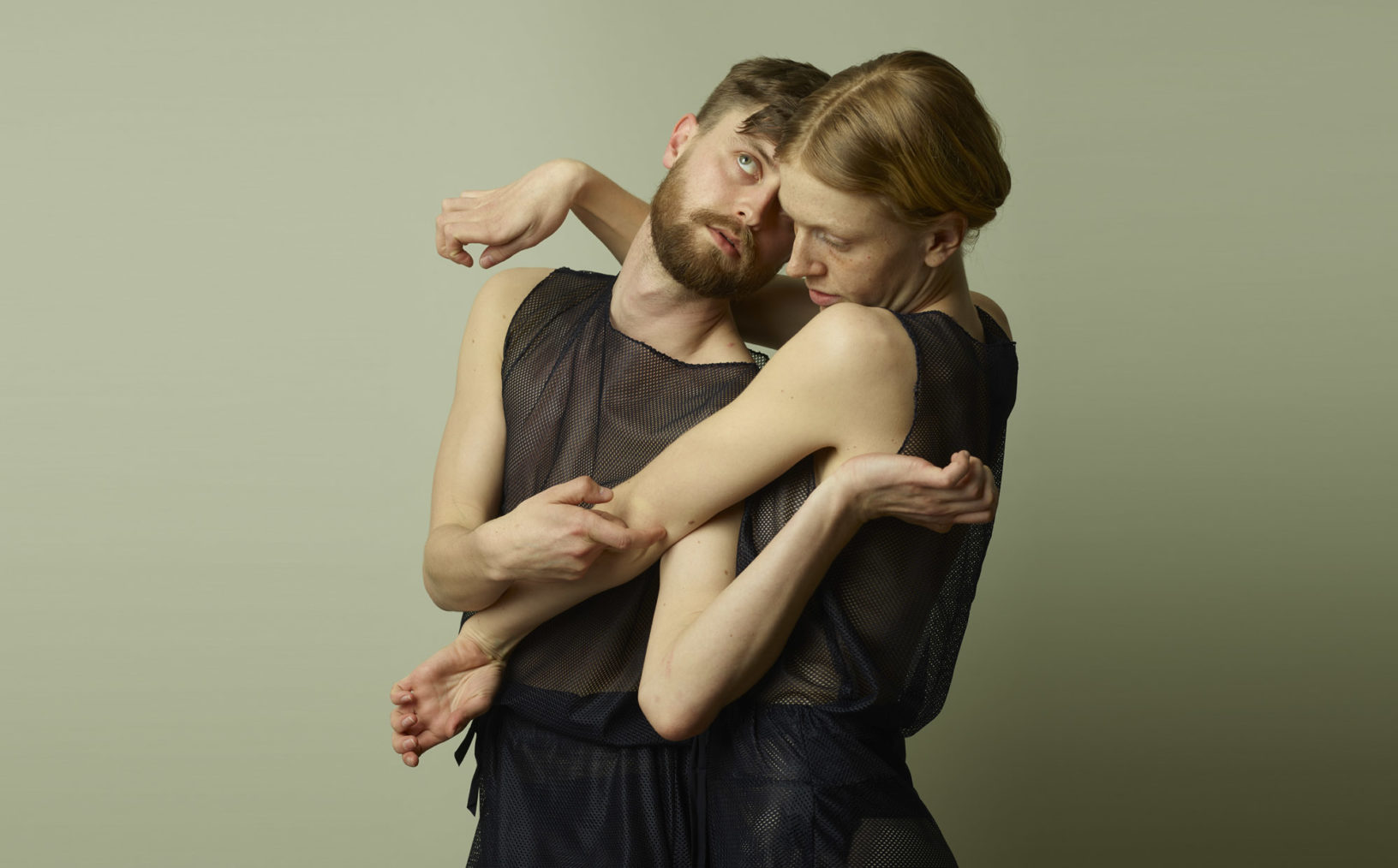 De to danserne i en positur fra forestillingen der de omfavner hverandre med armer og hender i vridde stillinger.