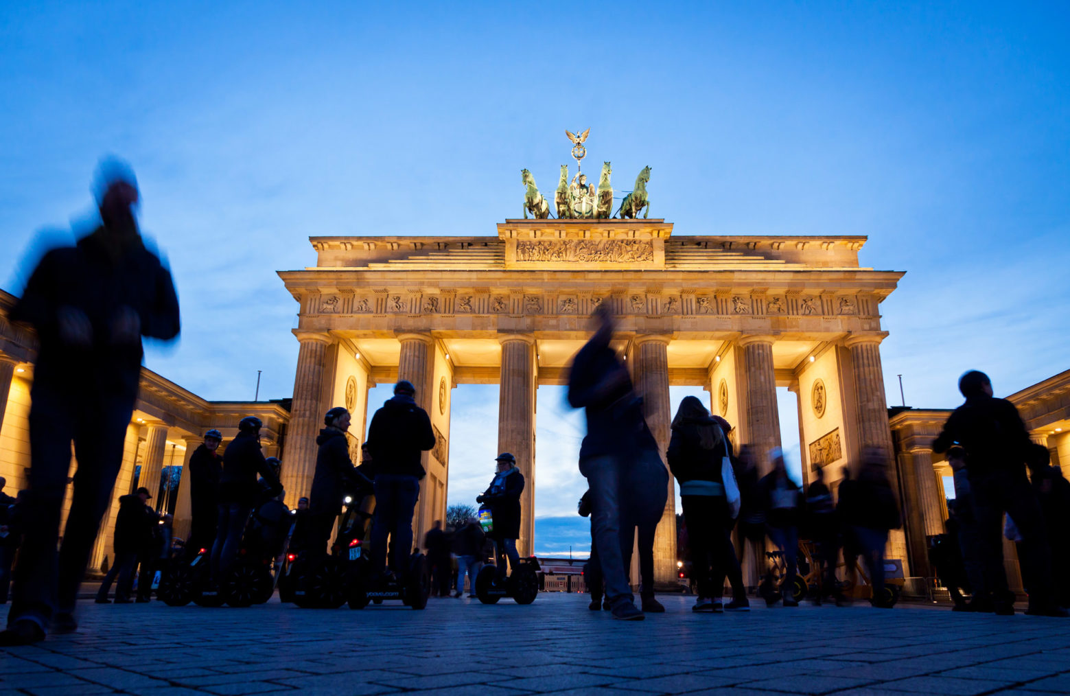 Siluetter av mennesker foran et flombelyst Brandenburger Tor.