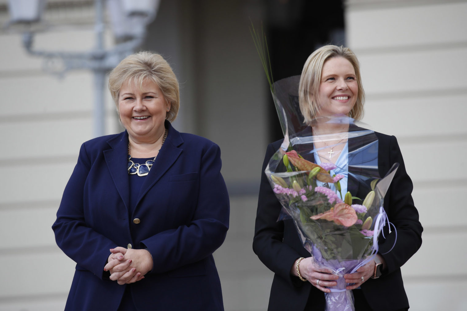 Erna Solberg og Sylvi Listhaug smilende på slottsplassen. Sylvi med blomster.