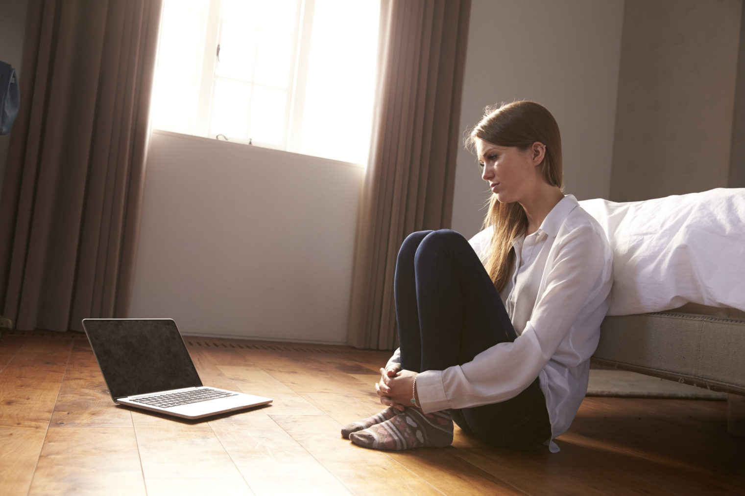 Illustrasjonsbilde av ung kvinne som sitter på gulvet og ser skremt mot en pc-skjerm.