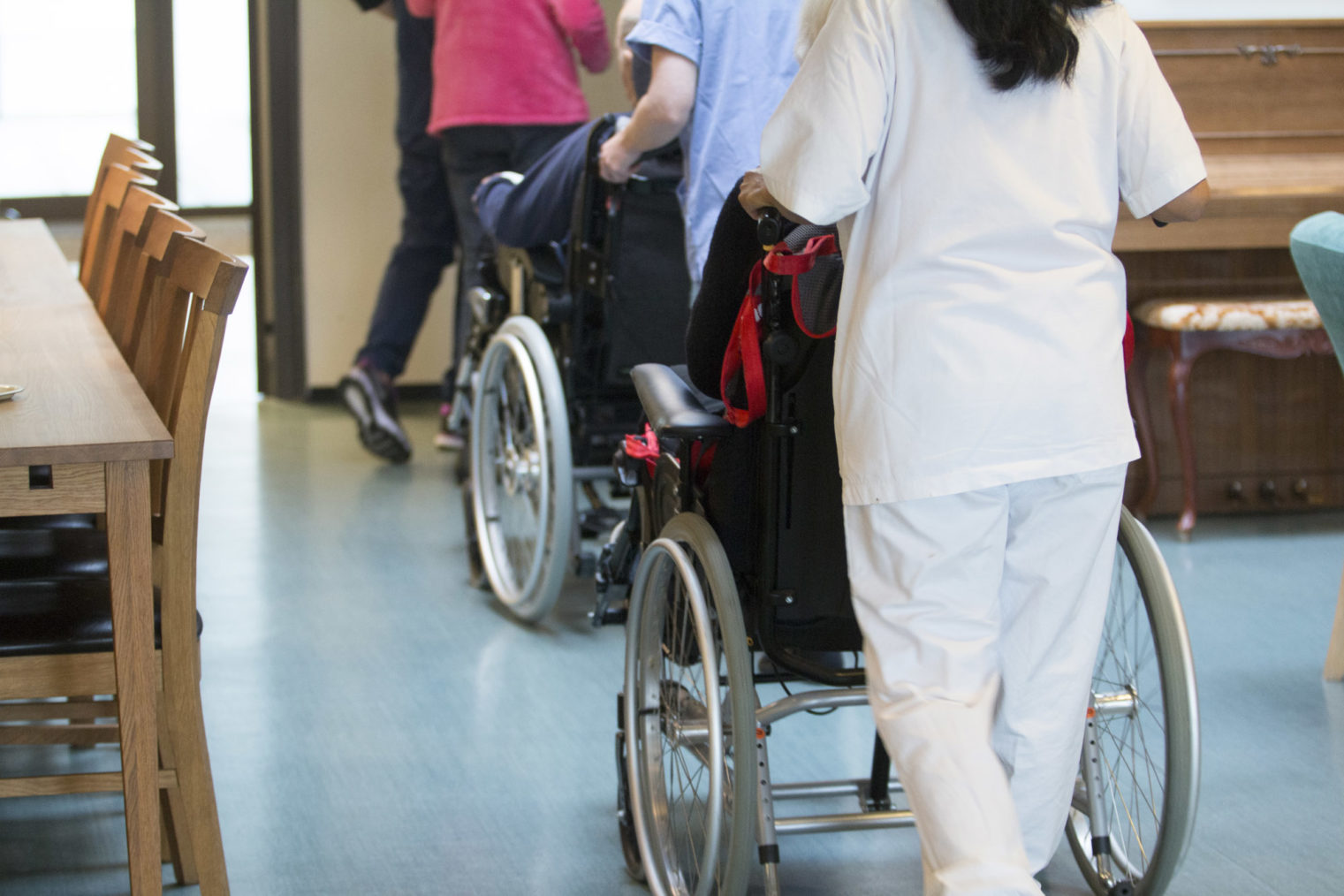 Illustrasjonsbilde av pleiere som triller rullestoler på et sykehjem.