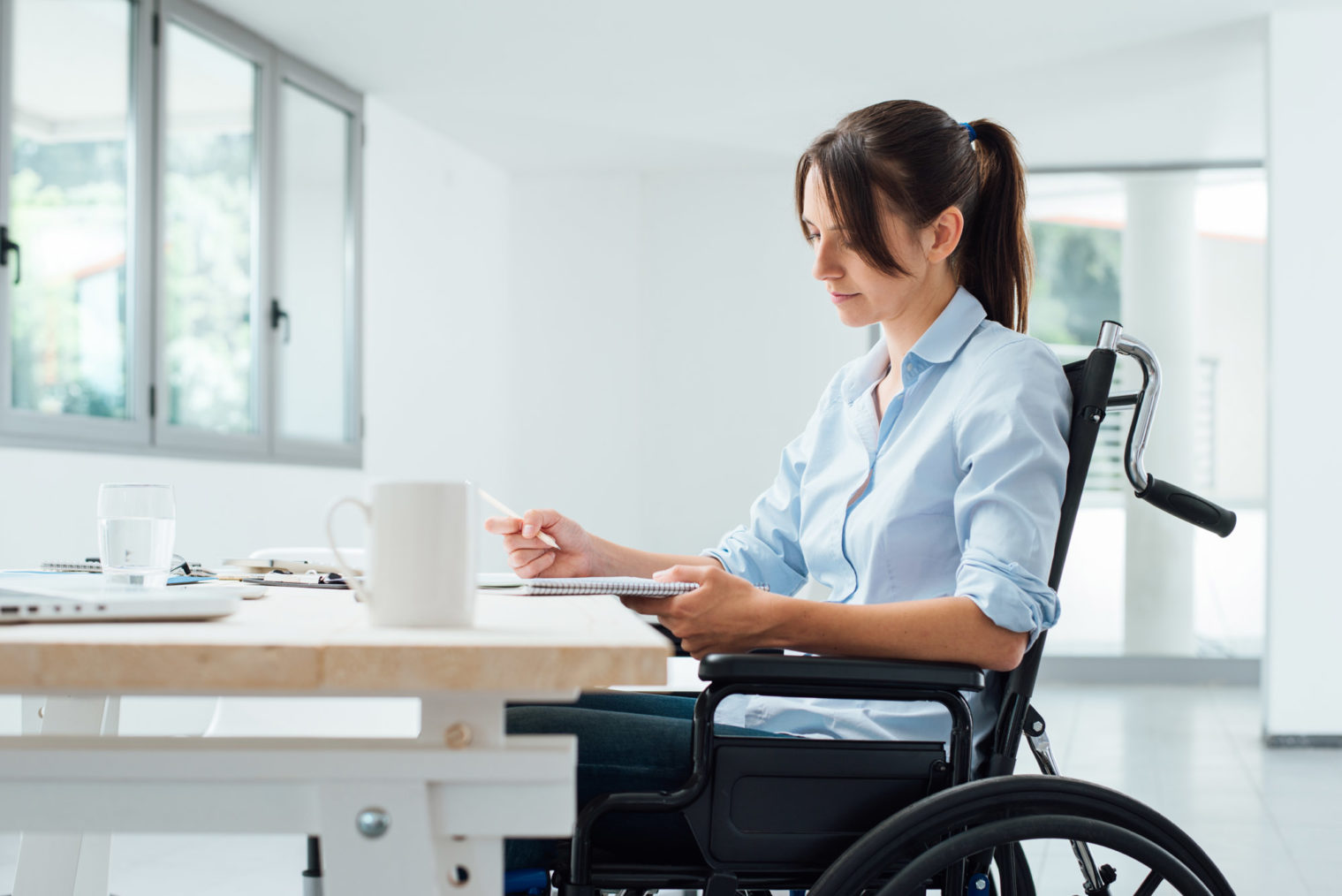 Bilde av ung kvinne i rullestol som driver med kontorabeid.